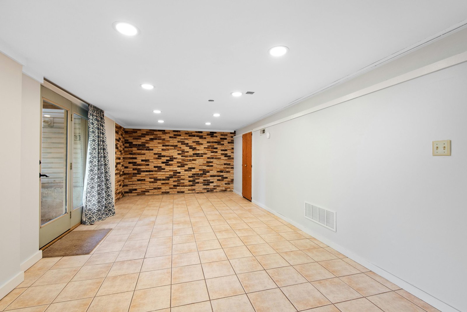 Bright and empty basement with brick accent wall and tile flooring.